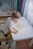 A boy, a child sits at a white table and reads a book. photo