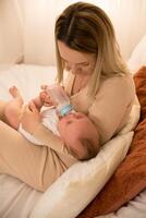 mom feeds a newborn baby with a bottle. the sun is shining in the background. photo