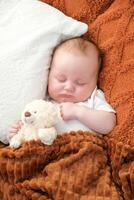 un recién nacido bebé duerme en un cama. un osito de peluche oso mentiras cercano. madre y niño. foto