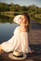 a beautiful girl in a hat stands on the shore. hat in hand. photo