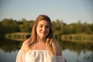 a beautiful girl is standing on the pier. in the background there is a river, a lake. photo