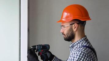 Man in uniform does pvc window installation with a screwdriver in office or apartment. video