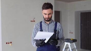 Man builder in uniform examining project documentation, repair works in apartment video
