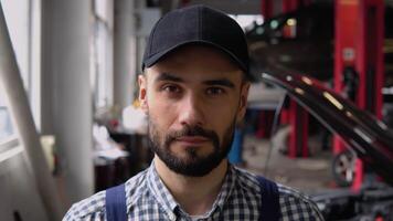 Portrait of a mechanic standing near broken car with open hood in a car repair shop video