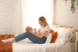 mom holds a newborn baby in her arms. in the background the sun shines from the window. photo