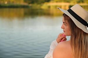 a beautiful girl in a hat stands on the shore. hat in hand. photo