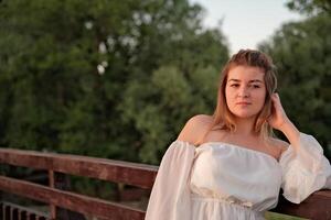 a beautiful girl in a white dress stands on a wooden bridge. photo