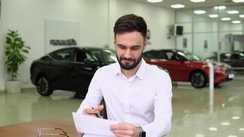 Autodiler making deal signs a sales document of a car while sitting at table in dealership office video