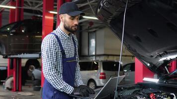 Man at the workshop in uniform using laptop for his job for fixing broken car video