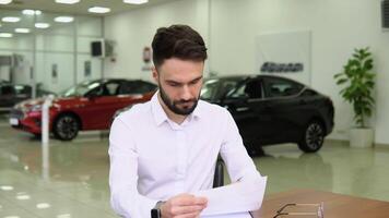 Autodiler making deal signs a sales document of a electric car while sitting at table in dealership office video