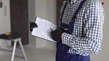 Man builder in uniform examining project documentation, repair works in apartment video