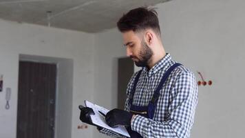 Man builder in uniform examining project documentation, repair works in apartment video