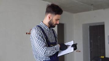 Young foreman builder, engineer or inspector checking and inspecting with clipboard at construction site building interior before complete new project. Contractor and engineering concept video