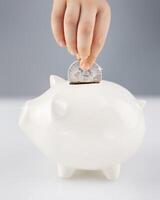 Child hand puts silver bitcoin coin in a white piggy bank photo