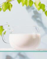 Glass cup of natural milk on a glass shelf with green branch photo