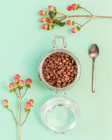 Coffee beans in a glass jar with spoon and red flowers photo