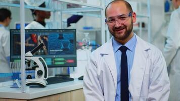 Microbiologist sitting in laboratory looking at camera in modern equipped lab. Multiethnic team examining virus evolution using high tech and chemistry tools for scientific research, vaccine development. video