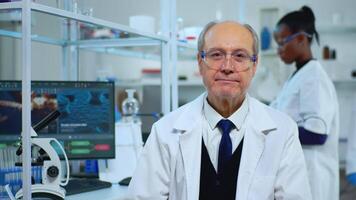 retrato do Senior com experiência cientista homem sorridente às Câmera dentro moderno equipado laboratório. multiétnico equipe examinando vírus evolução usando Alto tecnologia e química Ferramentas para científico pesquisar, vacina desenvolvimento. video