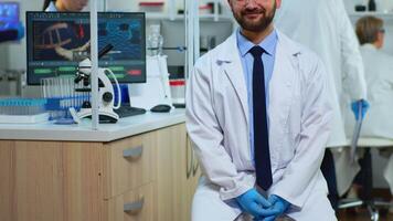 Experienced man scientist looking at camera smiling in modern equipped lab. Multiethnic team examining virus evolution using high tech and chemistry tools for scientific research, vaccine development video