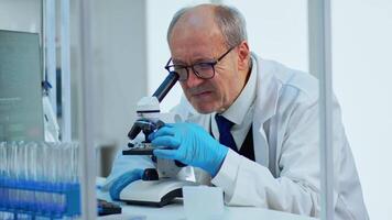 laboratório cientista conduzindo experimentar olhando às microscópio dentro ocupado moderno laboratório. idoso homem trabalhando com vários bactérias tecido, sangue amostras, conceito do farmacêutico pesquisa para antibióticos video