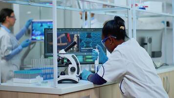Black woman chemist analysing reaction of virus on microscope in laboratory. Multiethnic team examining vaccine evolution using high tech for scientific research, treatment development against covid19 video