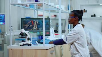 African doctor woman smiling at camera while working at pc in moder laboratory. Multiethnic team examining virus evolution using high tech and chemistry tools for scientific research, vaccine development video