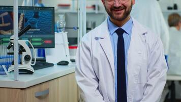 Portrait of scientist man smiling at camera sitting in modern equipped laboratory. Multiethnic team examining virus evolution using high tech and chemistry tools for scientific research, vaccine development. video