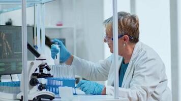 Senior scientist woman pipetting liquid to test tube in modern equipped lab. Multiethnic team examining virus evolution using high tech for scientific analysis of treatment development against covid19 video
