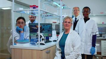 Team of multiethnic scientists sitting in laboratory looking at camera in modern equipped lab. Group of doctors examining virus evolution using high tech for scientific research, vaccine development. video