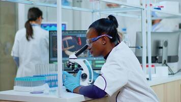 African woman scientist using microscope in modern equipped lab. Multiethnic team examining virus evolution using high tech for scientific research of treatment development against covid19. video