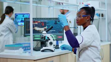 African scientist checking sample of virus using microscope in modern lab. Multiethnic team examining vaccine evolution using high tech for scientific research of treatment development against covid19 video