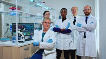 Multiethnic team of experienced scientists looking at camera in modern equipped lab. Group of doctors examining virus evolution with high tech and chemistry tools for scientific research, vaccine development of covid19 video