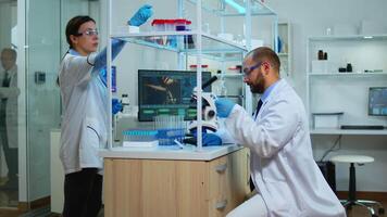 Scientist working in modern equipped laboratory cheching virus development with microscope. Multiethnic team examining vaccine evolution using high tech and chemistry tools for scientific research. video