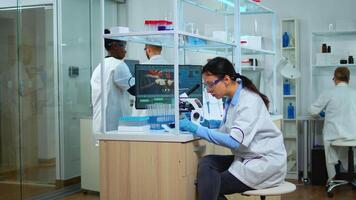 Microbiologist working for new vaccine in modern laboratory looking at samples under microscope. Multiethnic team examining virus evolution using high tech and chemistry tools for scientific research. video