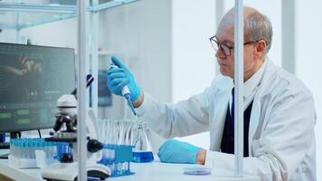 Elderly man scientist using micropipette for filling test tubes in modern equipped laboratory. Multiethnic team examining virus evolution using high tech for vaccine development against covid19 video