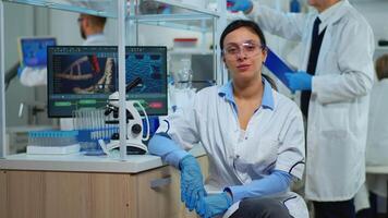 Tired laboratory doctor looking at camera smiling in modern equipped lab. Multiethnic team examining virus evolution using high tech and chemistry tools for scientific research, vaccine development. video