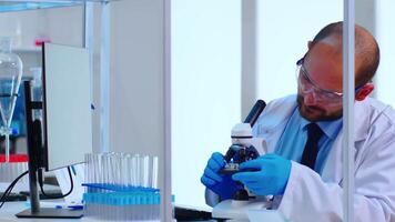 Medical research scientist conducting vaccine development under digital microscope in a biological applied science laboratory. Caucasian lab engineer in white coat working on medical treatment video