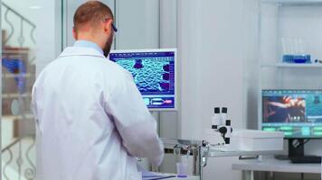 Professional chemist analysing vaccine development using touchscreen display in modern equipped laboratory. Man examining virus evolution using high tech researching diagnosis against covid19 video