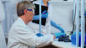 Senior biochemist typing and looking on pc analysing medical reports in modern equipped laboratory. Multiethnic stuff examining vaccine evolution using high tech researching treatment against covid19 video