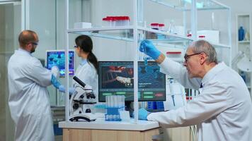 Elderly man technologist doing a laboratory test examining a flask with a blue substance, chemist holding tube with liquids inside. Scientist working with various bacteria tissue and blood samples video