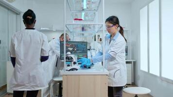 Woman scientist analyzing vaccine result in modern laboratory with microscope. Multiethnic team examining vaccine evolution using high tech for research in treatment development against covid19 virus video