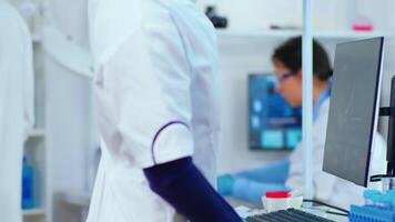 Black woman biologist researching using computer in modern equipped laboratory. Multiethnic stuff examining vaccine evolution using high tech and technology researching treatment against covid19 virus video
