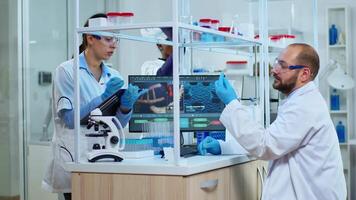 Multiethnic team studying DNA mutation, doctor checking tests from tubes while nurse taking notes on clipboard. Scientists examining virus evolution using high tech for research of vaccine development video