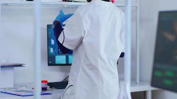 African chemist nurse writing on computer analysis results in modern equipped laboratory. Multiethnic doctors examining vaccine evolution using high tech researching diagnosis against covid19 virus video