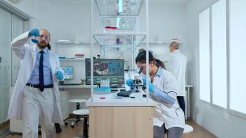 Chemist doctor checking liquid from tube test discussing with scientist nurse in modern equipped laboratory. Multiethnic team examining vaccine evolution using high tech for researching treatment video