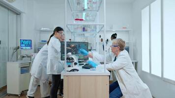 Multiethnic team working in busy modern equipped laboratory wearing white coat. Diverse group of scientists analysing vaccine evolution using high tech for researching treatment against covid19 virus video