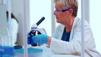 Senior scientist doing investigation using microscope in equipped laboratory. Multiethnic stuff examining vaccine evolution using high tech and technology researching diagnosis against epidemic virus video