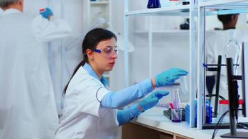 Woman scientist filling liquid test tube with pipette in modern equipped laboratory. Multiethnic medical stuff examining vaccine evolution using high tech researching diagnosis against covid19 virus video