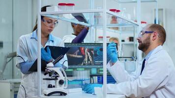 Diverse team of biochemistry scientists developing drugs agains new virus, doctor checking samples while nurse taking noters on clipboard in modern equipped laboratory. Multiethnic scientists working video