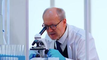 Senior laboratório técnico examinando amostras e líquido usando microscópio dentro equipado laboratório. cientista trabalhando com vários bactérias, lenço de papel e sangue amostras, farmacêutico pesquisa para antibióticos video